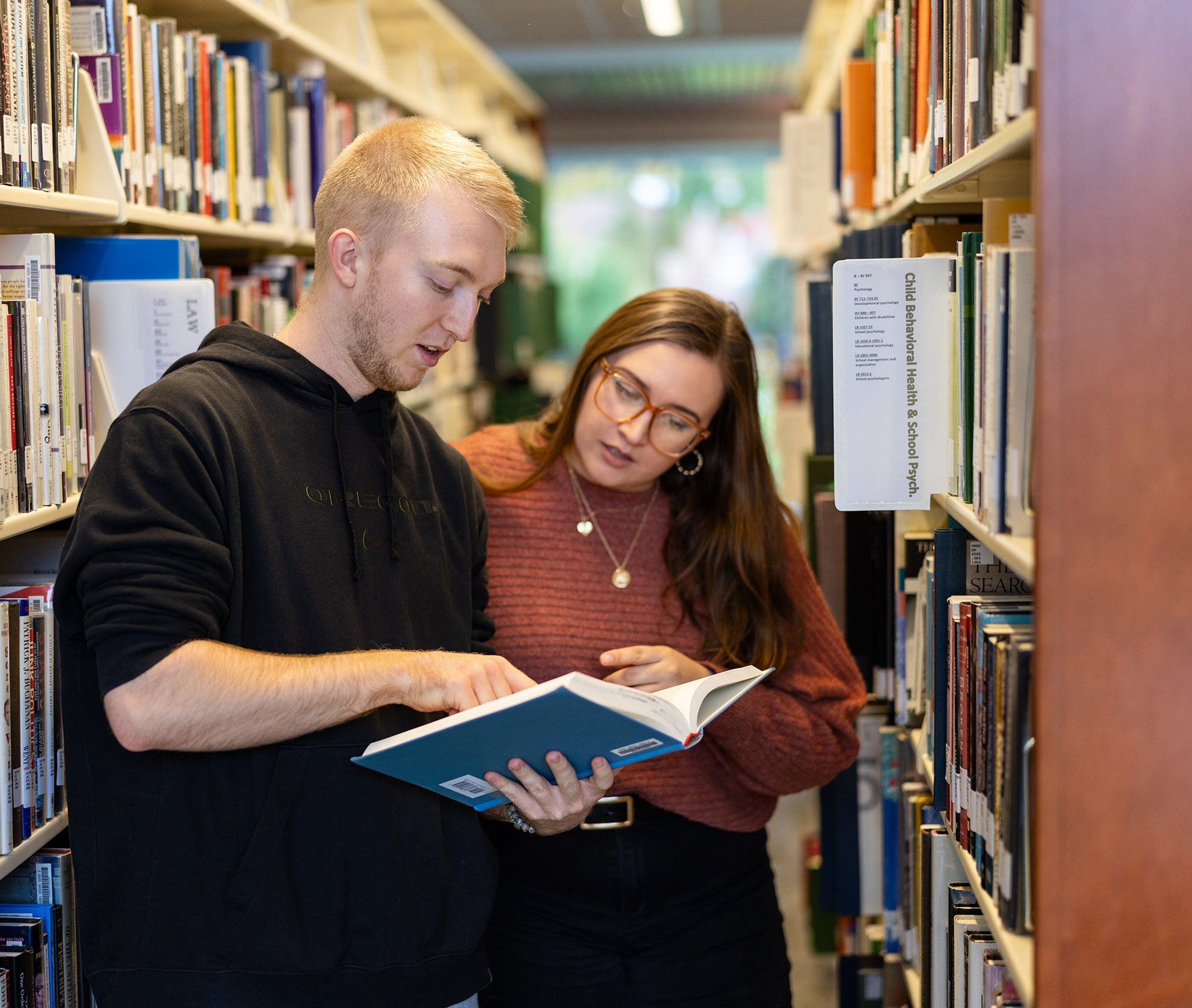two students read a book amid library shelves