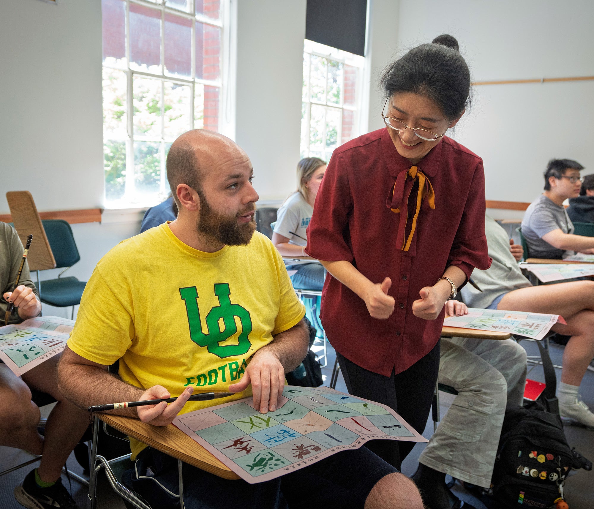 A professor talks to a man as he works on calligraphy.  